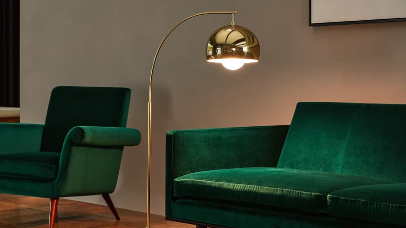 Lampada da terra ad arco in ottone accanto a un divano in velluto verde