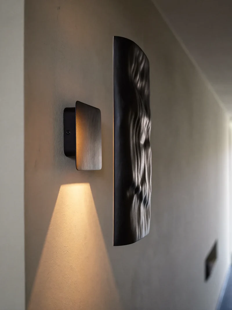 Applique nera opaca che proietta un cono di luce su una parete intonacata